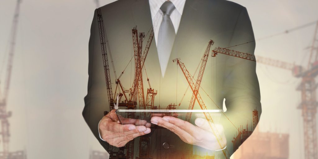 Double exposure of businessman hand hold tablet, construction crane, building and sunset in the evening as business, technology, communication and industry concept.