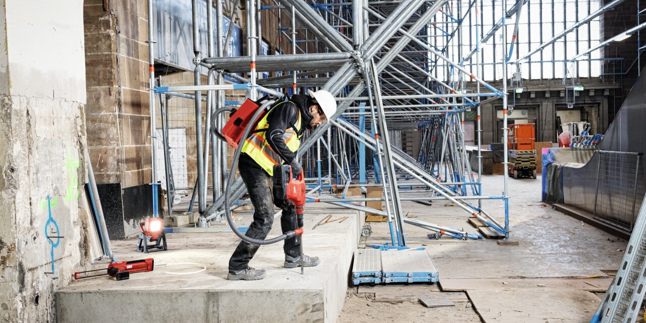 Construction worker using Hilti tool connected to a vaccuum cleaner