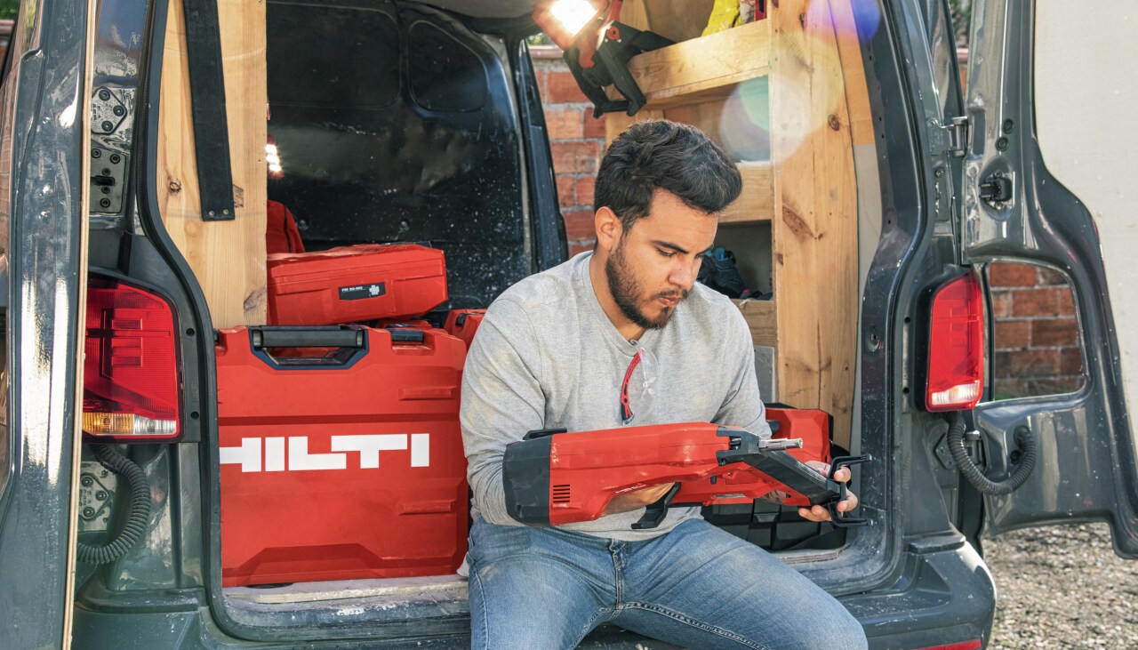 Un homme assis à l'arrière de sa camionnette avec un cloueur dans les mains