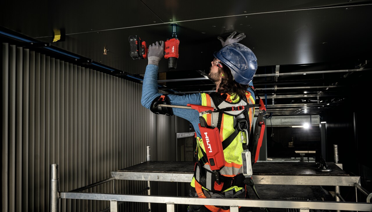 Travailleur avec exo-squelette et visseuse sans fil lors de travaux au plafond