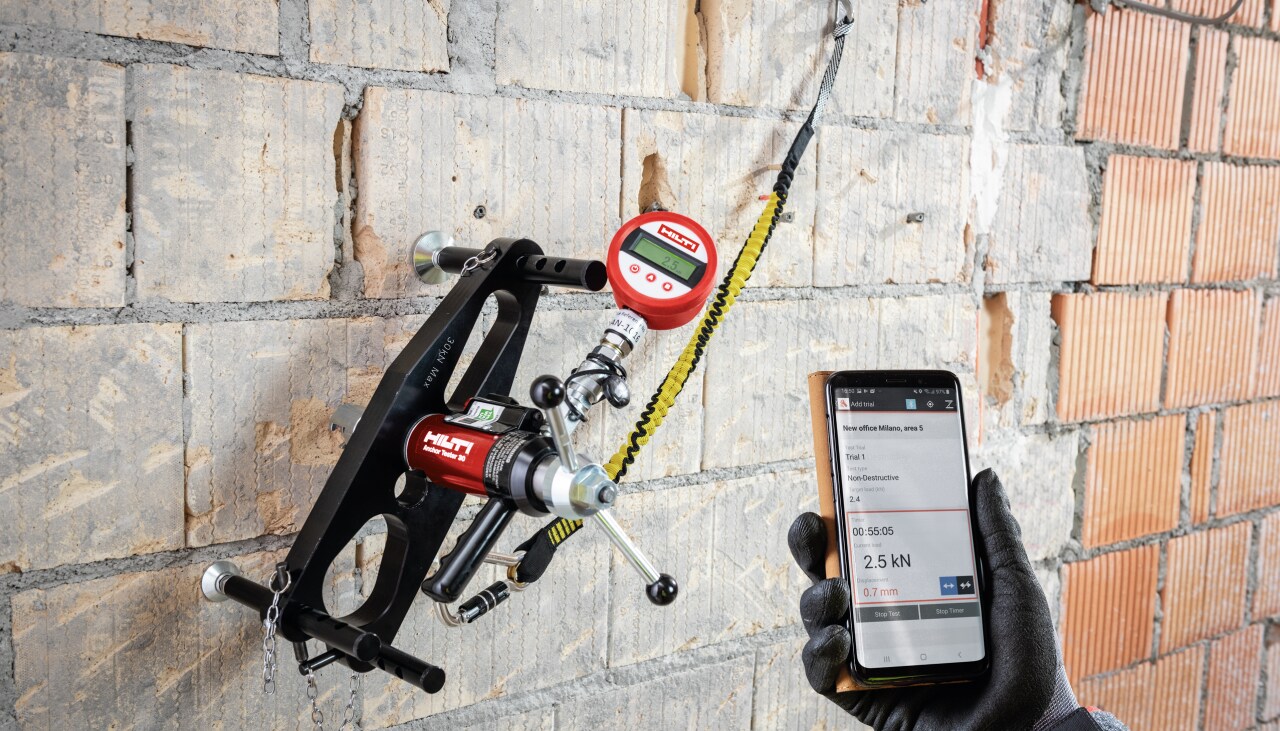 Hilti darbuotojas naudoja hilti įrankį, laikydamas telefoną