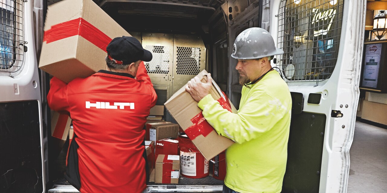 Du darbuotojai neša dėžes iš mašinos bagažinės